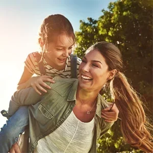 Chiropractic Kissimmee FL All Ages Welcome A young girl riding on her mother's shoulders and laughing on a sunny day