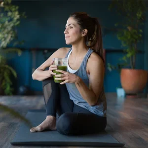 A woman holding a green smoothing and stretching after yoga